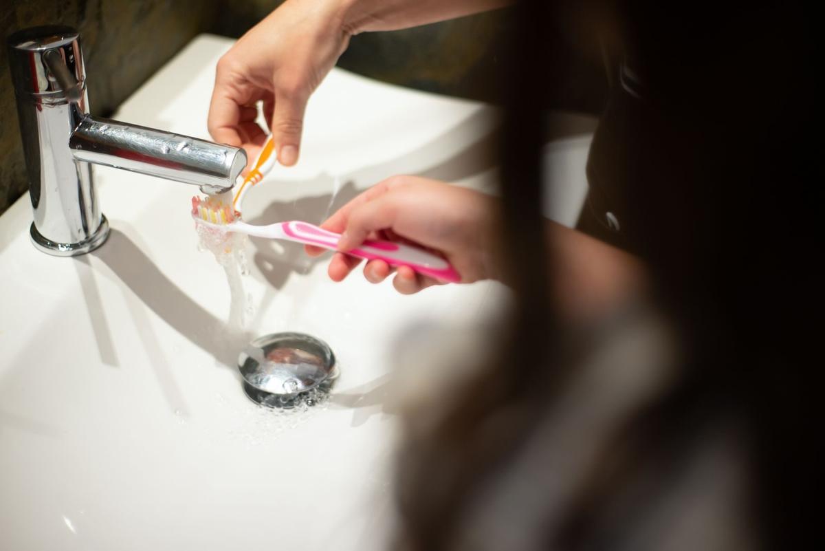 Mała dłoń trzymająca szczoteczkę do zębów nad umywalką